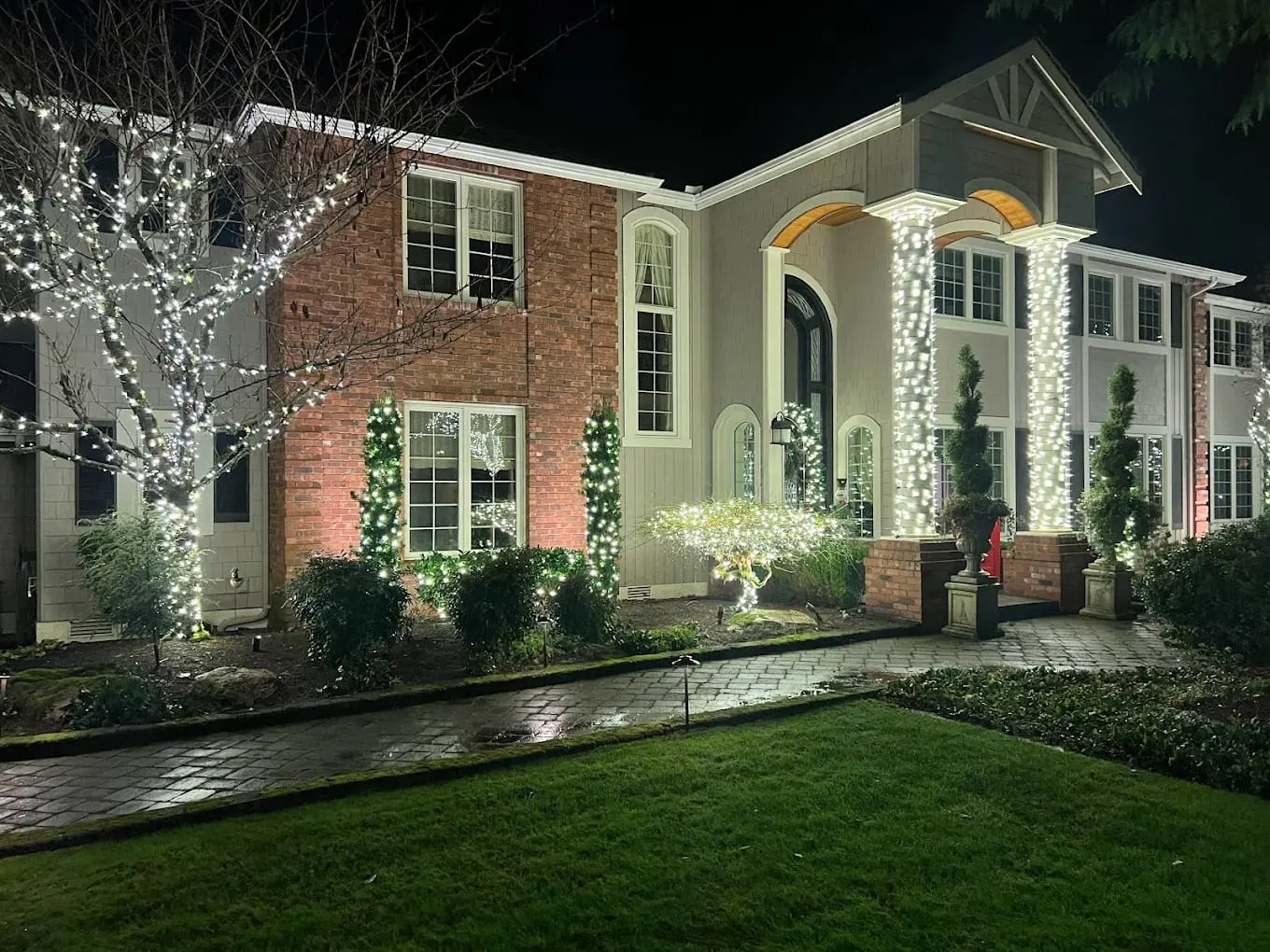 Estate with custom lighting, wrapped trees, column accents, and landscape features